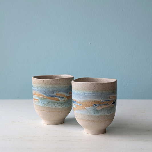 Two beige ceramic cups with light blue glaze