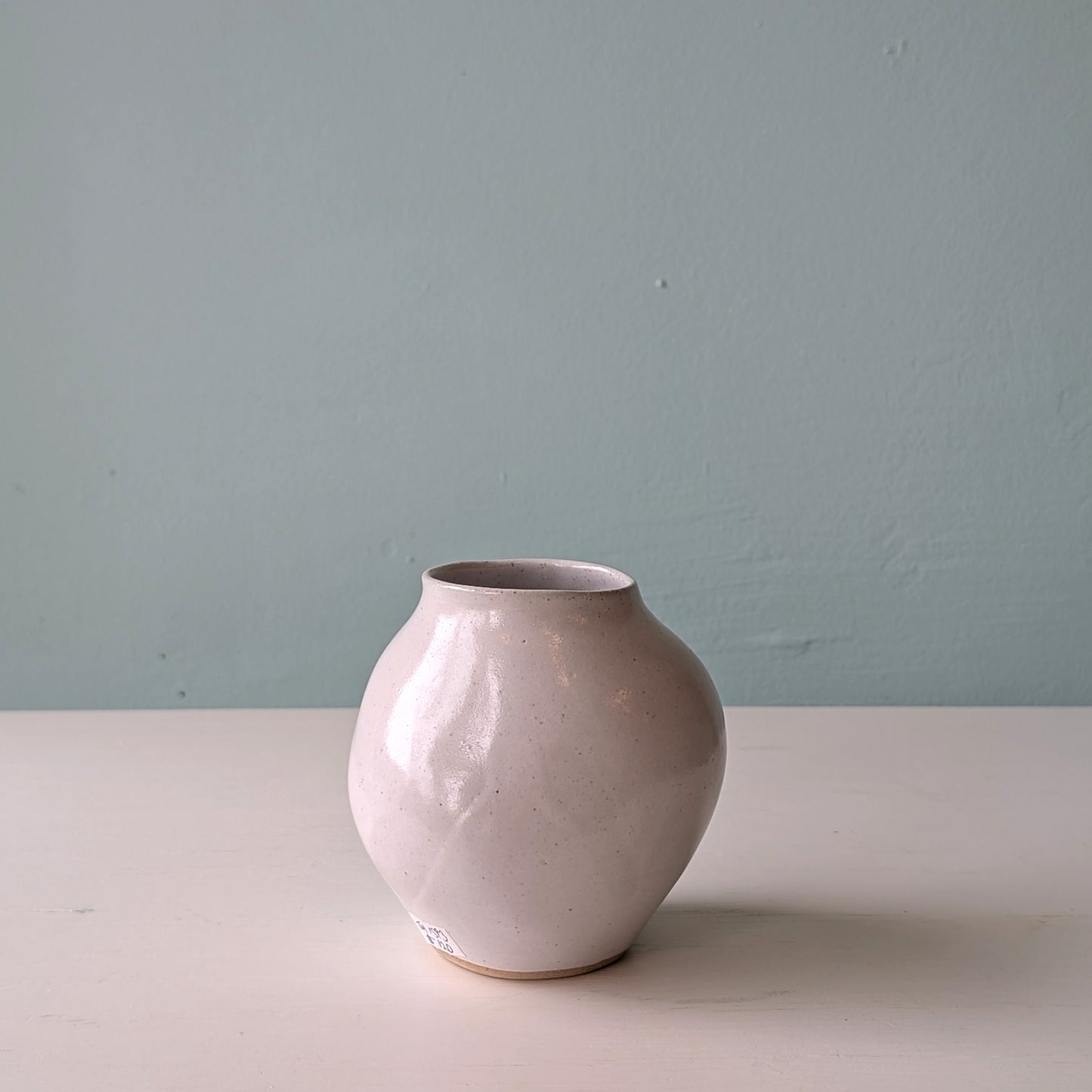 Beige ceramic vase on a white surface with a light blue wall background