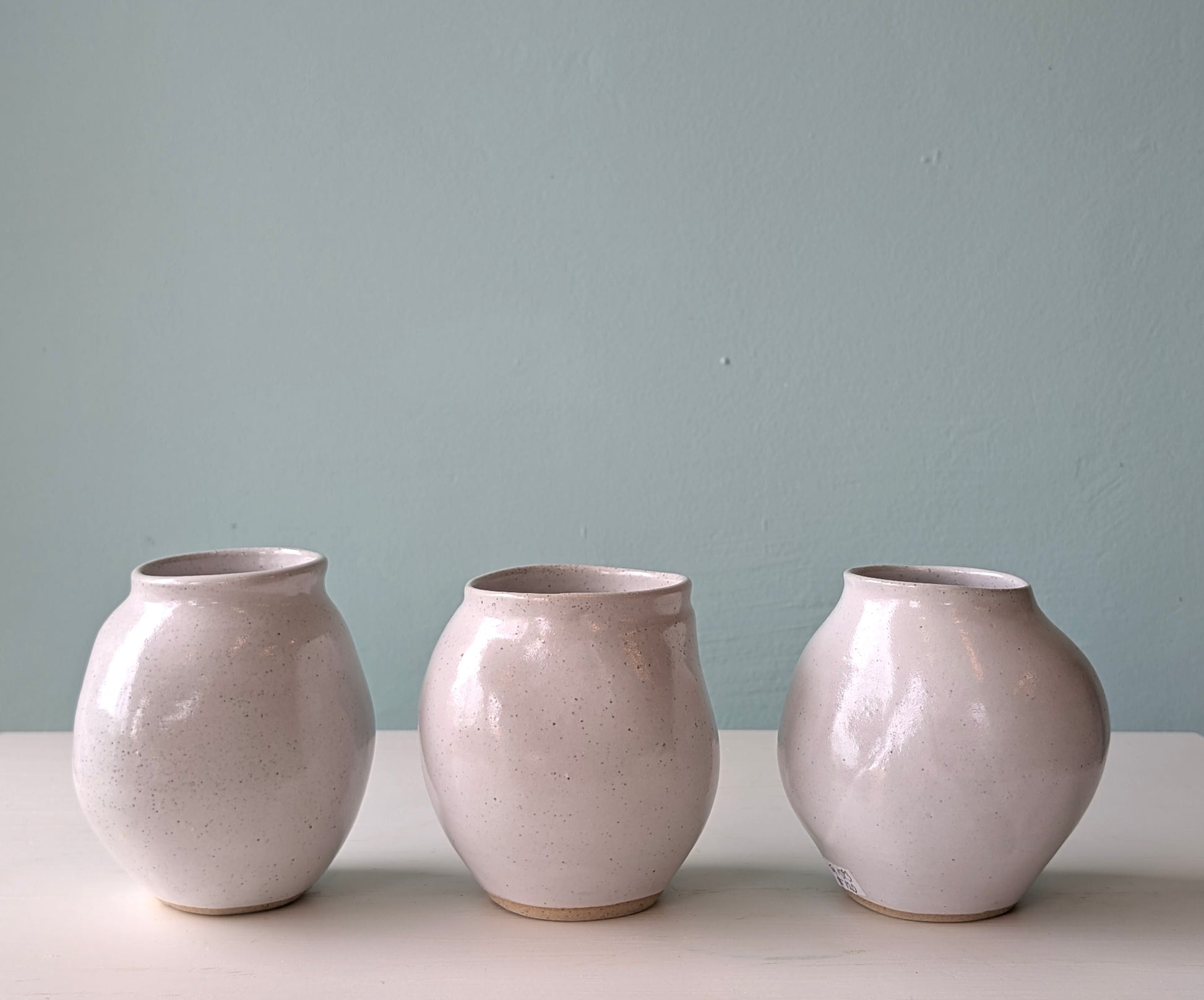 Three ceramic vases of similar design on a light surface with a light blue wall background