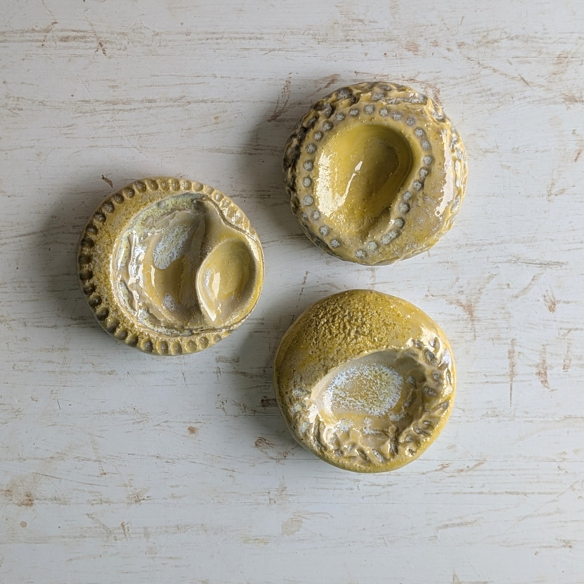 Three yellow ceramic sculptures with textured surfaces on a light wooden background