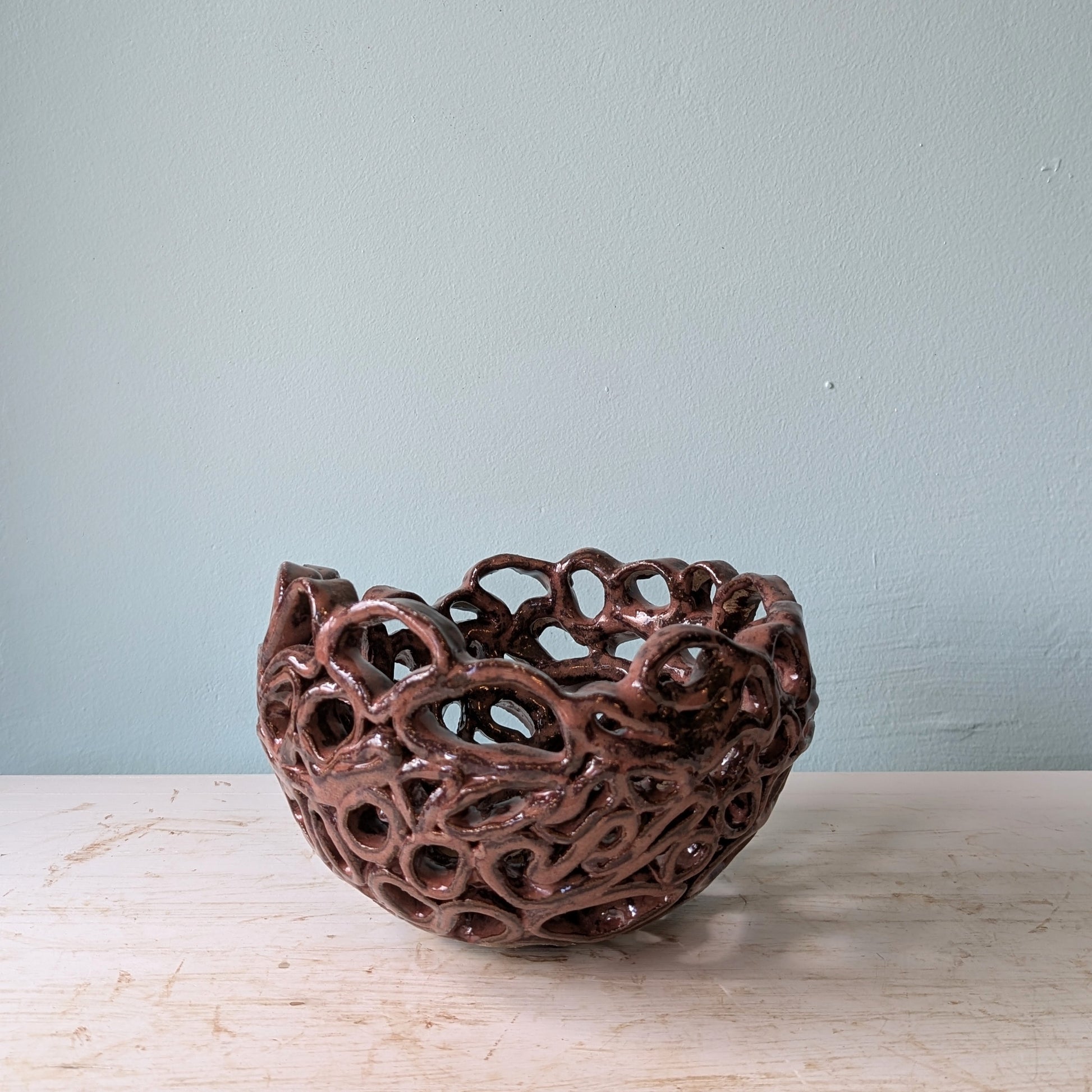 Brown ceramic bowl with perforated design on a white table against a blue wall.