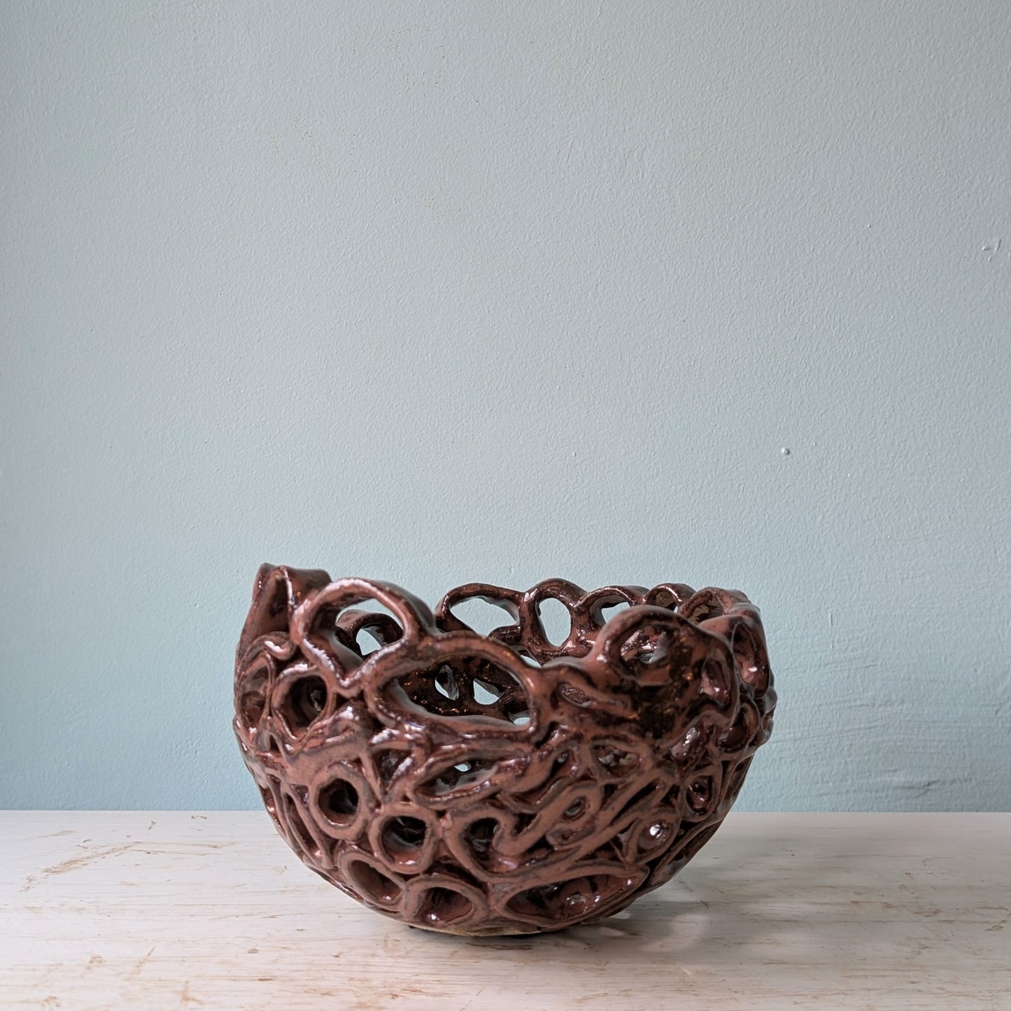 Brown ceramic bowl with perforated design on a white table against a blue wall.