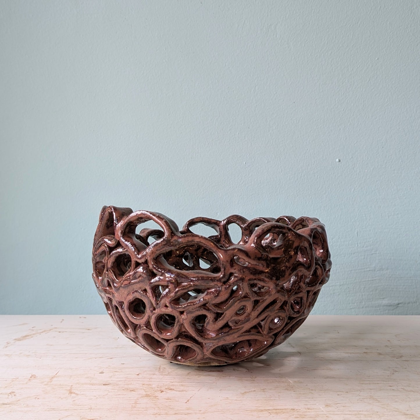 Brown ceramic bowl with perforated design on a white table against a blue wall.