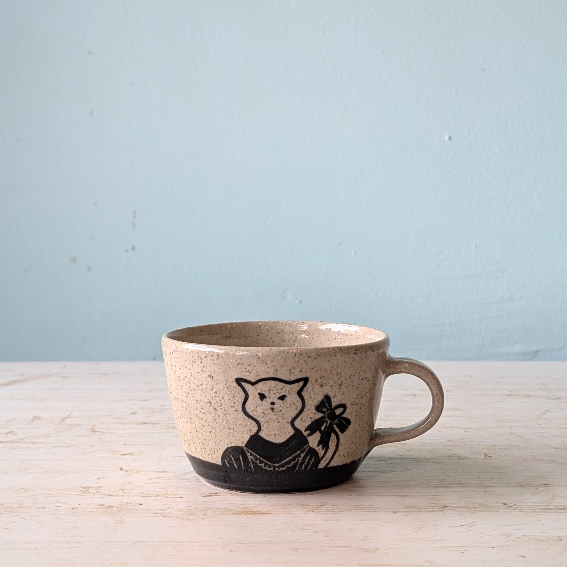 Ceramic mug with a cat illustration on a light wooden surface and blue background