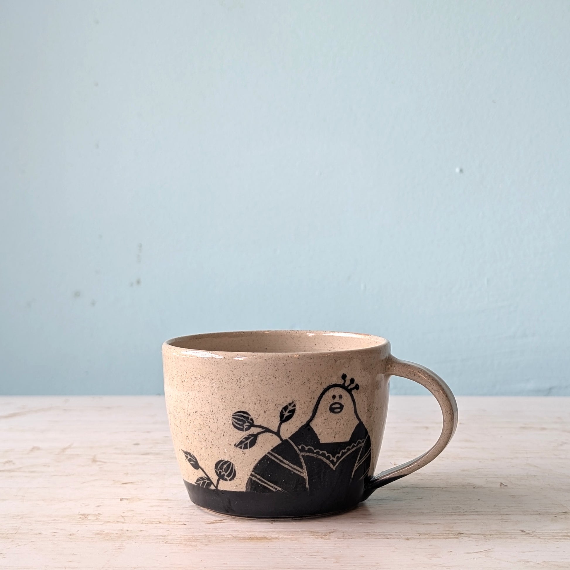 Ceramic mug with a black illustration of a peacock on a light blue background