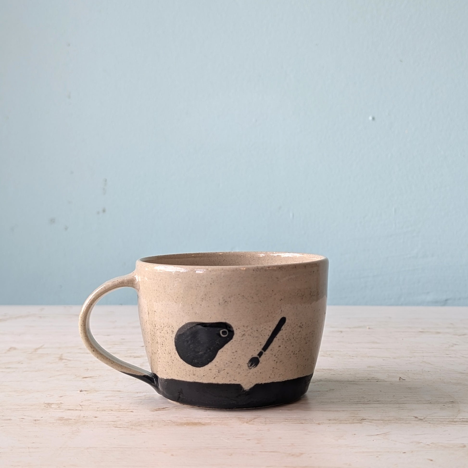 Ceramic mug with a black design on a light wooden surface and light blue background