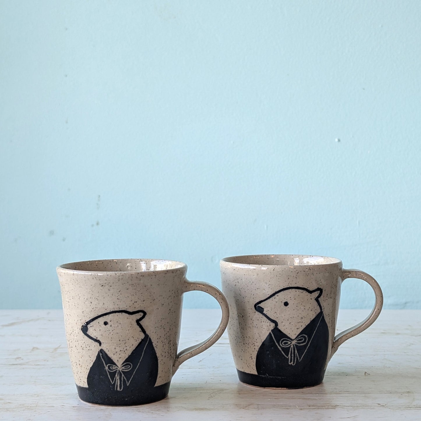 Two ceramic mugs with bear illustrations on a light blue background