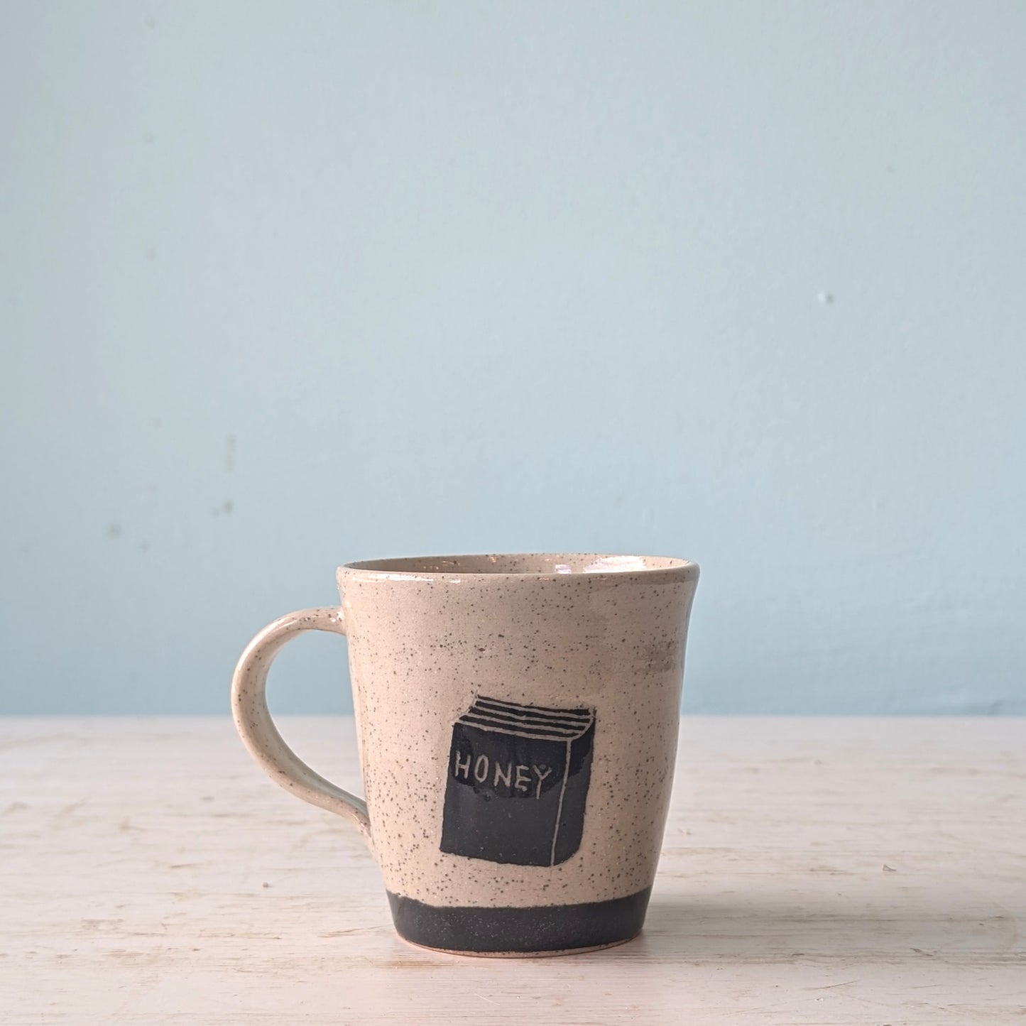 Ceramic mug with 'honey' design on a light wooden surface and blue background