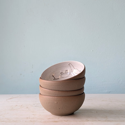 Stack of four ceramic bowls on a light wooden surface with a light blue background