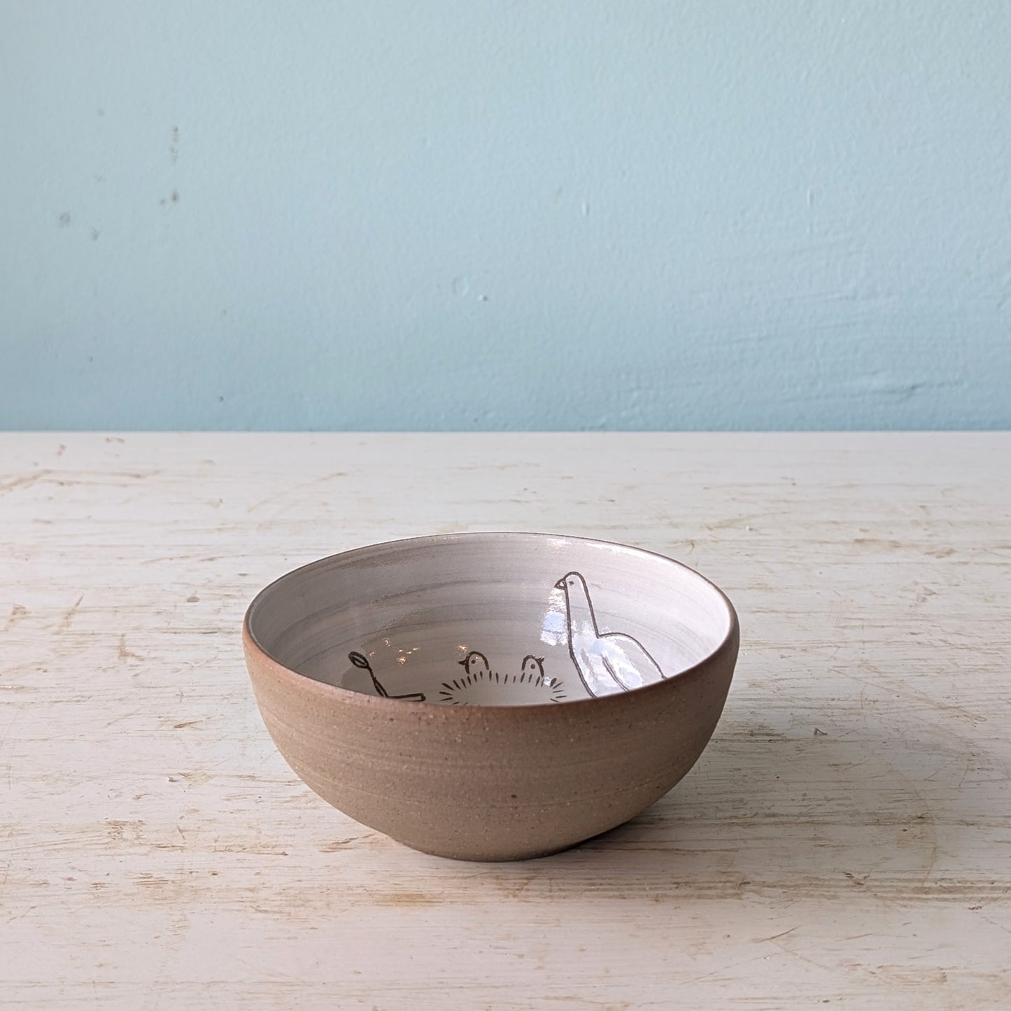 Ceramic bowl with a bird design on a wooden surface and light blue wall background