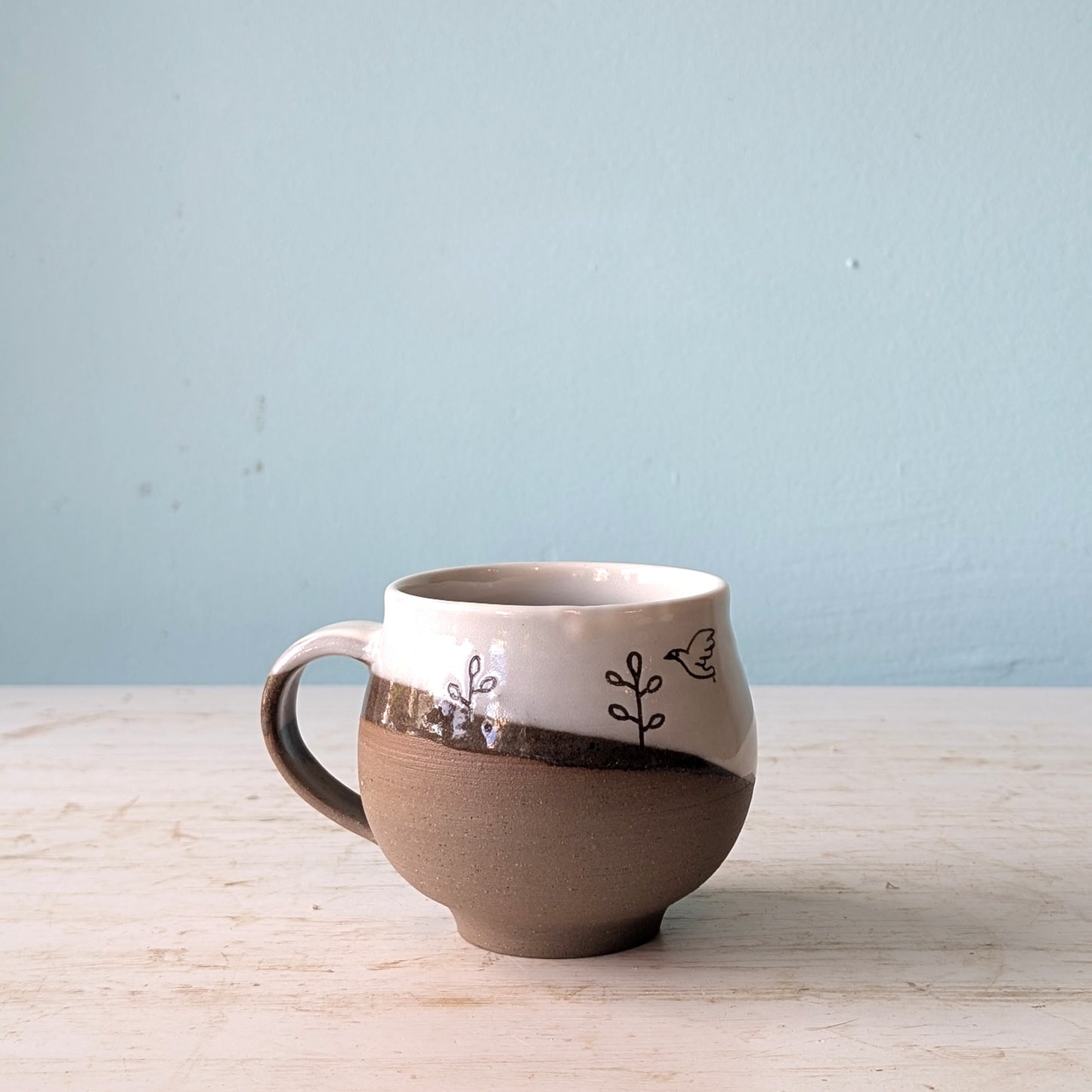 Ceramic mug with decorative elements on a light wooden surface and blue background