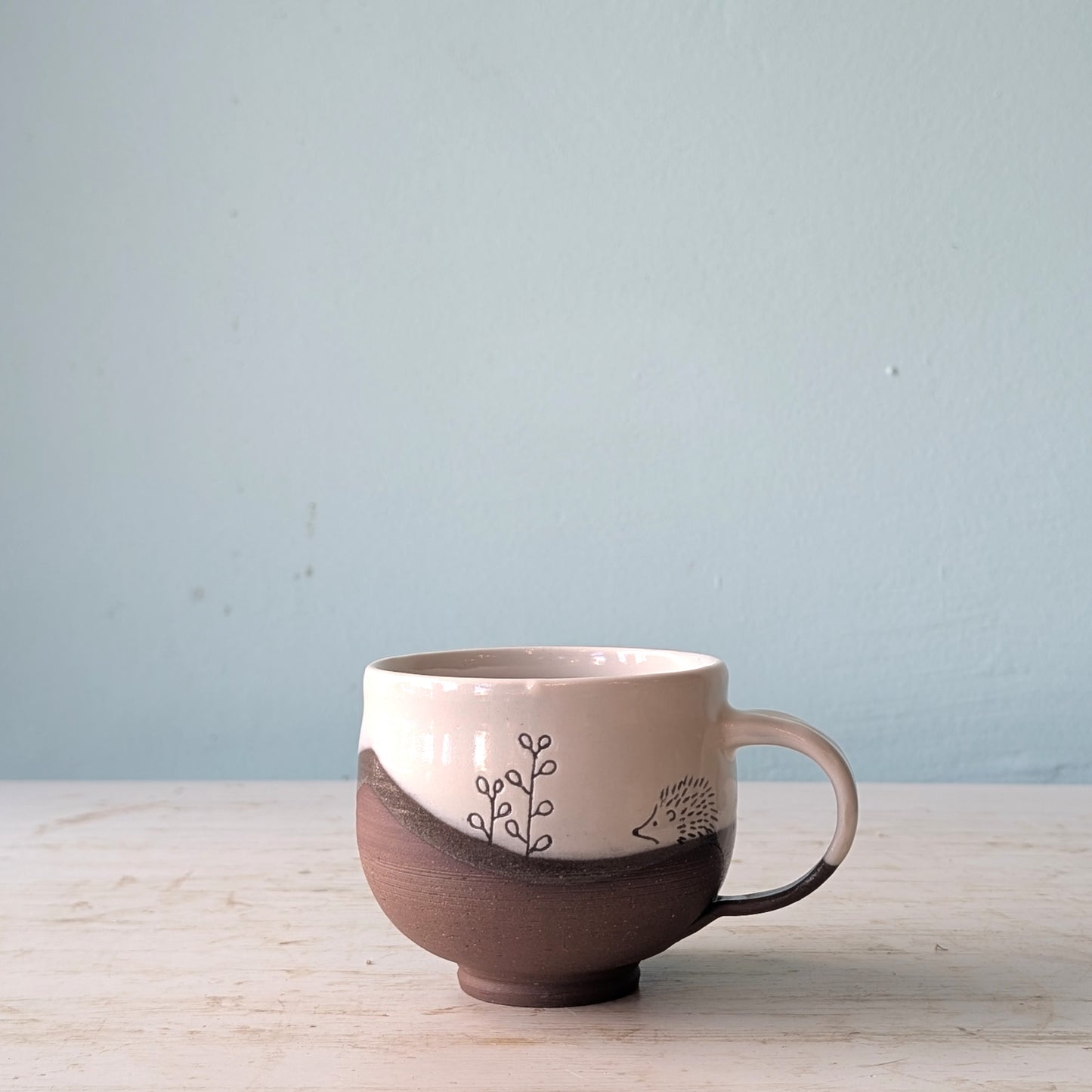 Ceramic mug with hedgehog design on a light wooden surface and light blue background